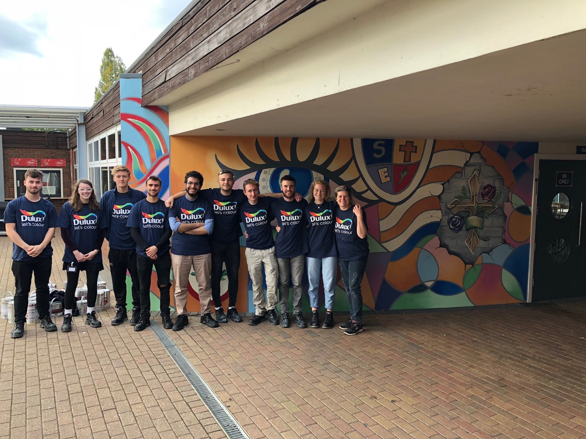 Group of 10 volunteers in Dulux branded t-shirts next to painted school mural.