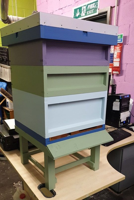 An upcycled painted beehive in pale pink paint, purple paint, green paint and light blue paint using low cost and recycled paint from Community RePaint Bradford.