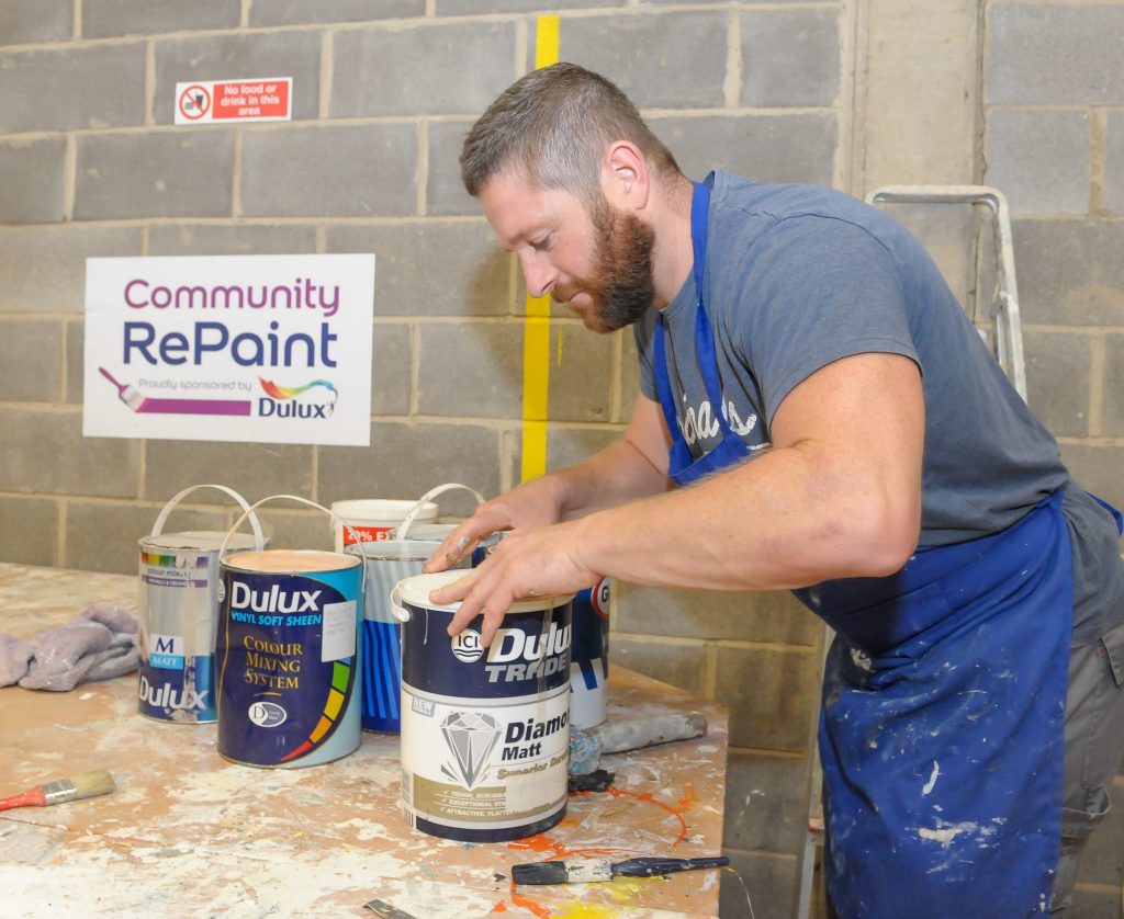 A member of staff at the Community RePaint Loughborough scheme in a workshop processing paint ready for resale. He is in the process of returning a lid to a container of Dulux Trader Diamond Matt.