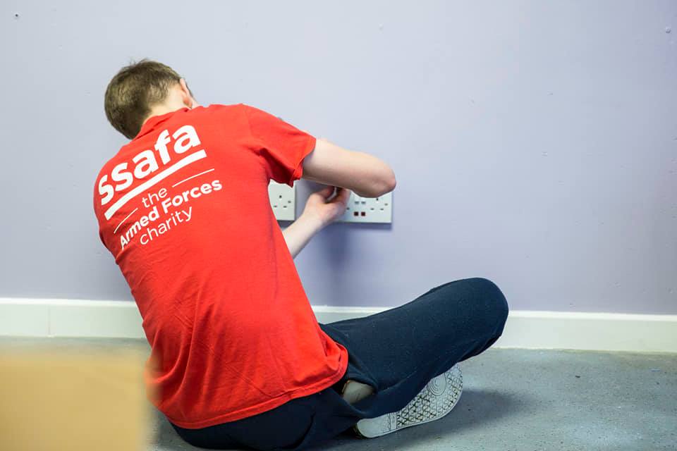 A volunteer paint removes masking tape off a plug point after a room has been redecorated using low cost ReColour matt emulsion in a light purple.