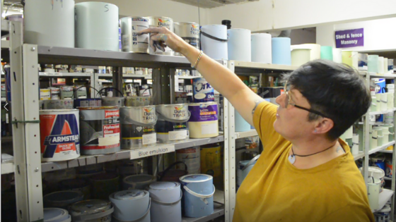 Staff member at Community RePaint Bradford scheme looking at shelves full of cheap and recycled paint for sale to the community.