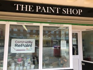 The shop front of The Paint Shop, the Community RePaint Northampton scheme. In the window is the Community RePaint logo and a few paint containers.